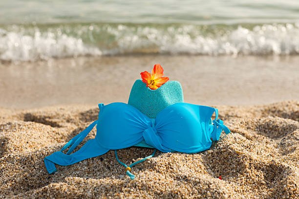 Turquoise summer hat, bikini and flower on the beach stock photo