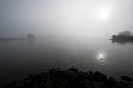 Fisherman observes the sunset on the shore of a lake. View from behind and copy space. Angler is fishing with the carpfishing technique using special equipment such as rod pod and electronic bite alarms