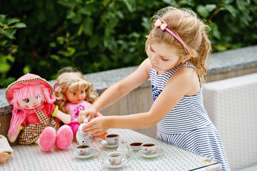 Little preschool girl playing with dolls. Happy excited child play tea party with toys. Role games for children, activity for one person. Role game for small children