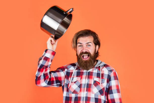 istock welcome in restaurant. Enameled cast iron cooking vessels. Nonstick pan coated polytetrafluoroethylene teflon. Cooking healthy food. Professional chef man cook in checkered shirt. bearded husband 1468176083