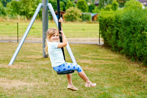 Happy kid girl rids on zip line swing outdoor game play equipment on playground. Child having fun outdoors. Preschool child swinging on summer day. Activity with children