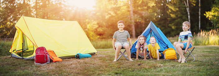 Group of children resting in the campground in nature. Concept of the family vacation, recreation and scouts camping.