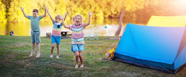 Group of four children playing near colourful tents in nature. Concept of the family vacation, recreation and scouts camping.
