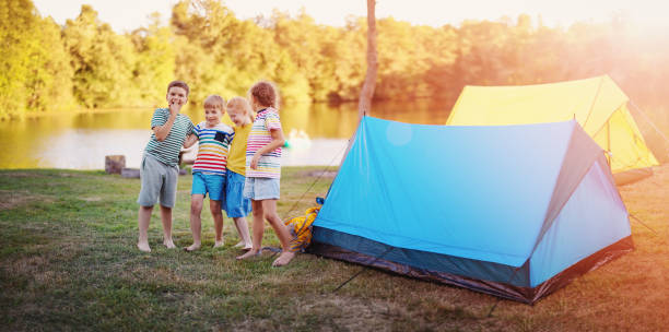 Group of four children standing near colourful tents in nature. stock photo