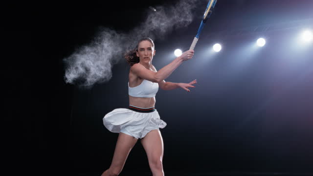 Aesthetic Shot of an Athletic Female Tennis Player with a Black Background Hitting the Ball Under Spotlights. Cinematic Super Slow Motion Captures a Winning Strong Forehand Shot with Smokey Effect