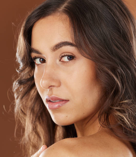 Woman, face skincare or curly hairstyle on brown studio background in color dye advertising, self love or Brazilian keratin treatment. Portrait, beauty model or brunette waves and natural makeup glow cuidado de la piel de la mujer, la cara o peinado rizado sobre fondo de estudio marrón en publicidad de tinte de color, amor propio o tratamiento de keratina brasileña. retrato, modelo de belleza u ondas morenas y maquillaje natural brillan