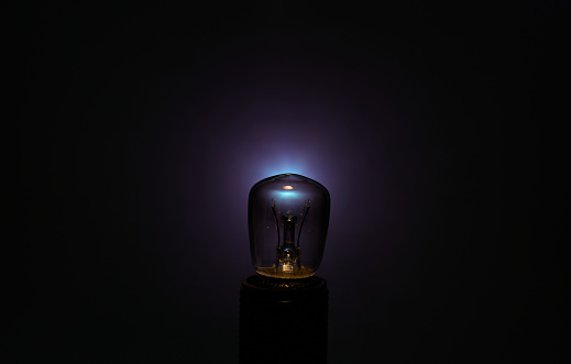 Small unlit incandescent bulb against a dark electric blue background