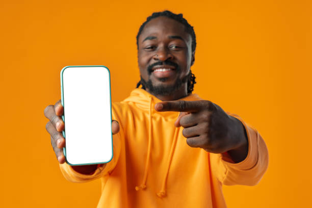 istock Smiling african man pointing at cellphone with blank screen with copy space 1468183945