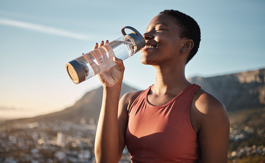 Black woman, runner and drinking water for outdoor exercise, training workout or marathon running recovery. African woman, healthy athlete and hydrate with bottle for fitness, health and cardio run