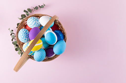 Pastel colored dyed Easter eggs in a basket on pink background