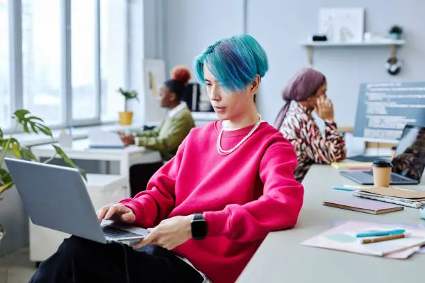 Photo of Asian young man using laptop in modern office, magenta accent