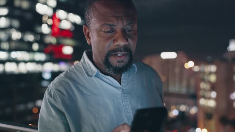 Businessman, phone and video call stress at night in New York city with work communication. Mistake, fail and anxiety of mature black man on urban balcony talking on mobile with bokeh lights.