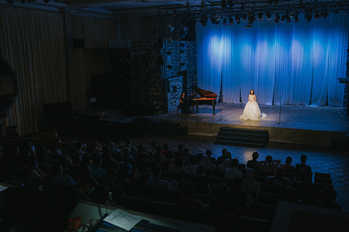Young Chinese Female opera singer performing solo on stage with Pianist in front of audience
