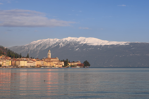 Winter sunset on promenade of the Salo town on Lake Garda against the backdrop of the snow-capped peaks of the Alpine mountains
