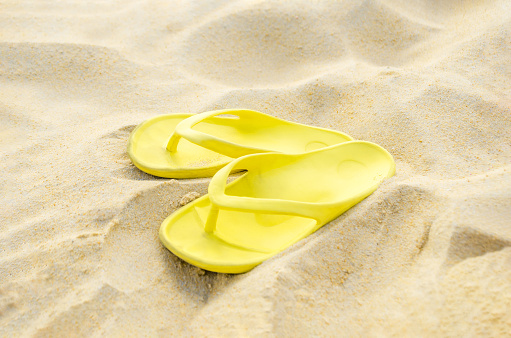 Yellow flip-flops on the sand. Sandals on the beach
