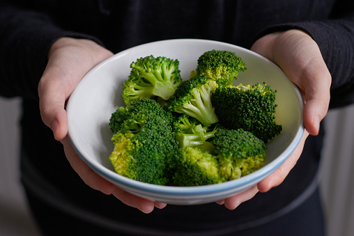 Hands holding a bowl of freshly steamed broccoli ready to eat