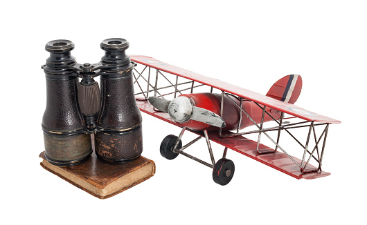 Old time-worn objects full of poetry, fun and adventure: a tin airplane, an old book with a leather cover and binoculars on top. Ready for adventurous travels!