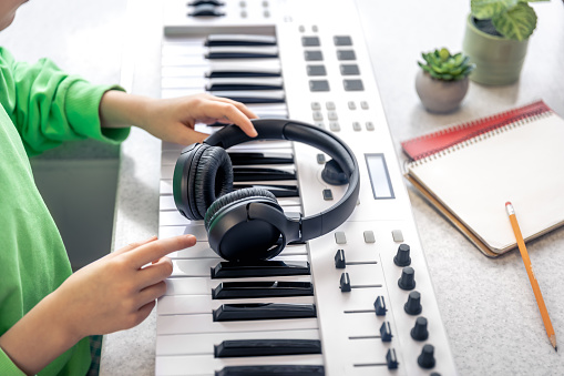 Close-up, black headphones in the hands of a child on the background of the piano.
