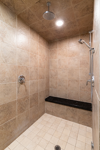 A brown tiled luxury shower with a chrome showerhead and black tiled bench seat.