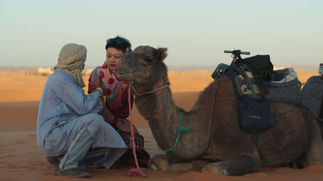 Moroccan Tour Guide showing camel to Asian Chinese female tourist in Sahara Desert