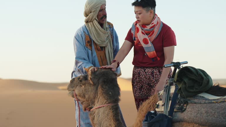 Moroccan Tour Guide showing camel to Asian Chinese female tourist in Sahara Desert