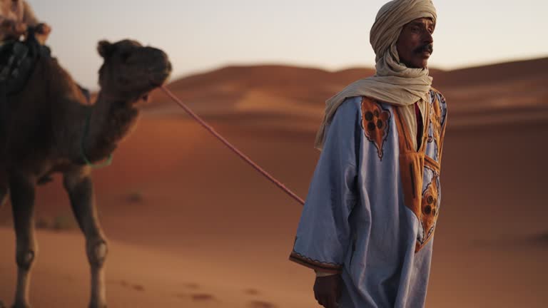 Asian Chinese Female Tourist Camel caravan going through the Sahara desert in Morocco at sunset