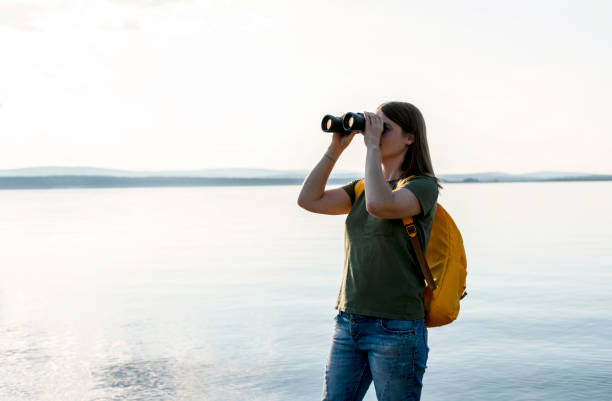 istock Young woman with yellow backpack looking through binoculars at birds on lake or river Birdwatching, zoology, ecology Research in nature, observation of animals Ornithology wildlife manager copy space 1468218400