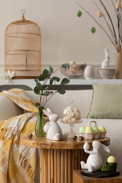 istock Spring composition of living room interior with round coffee table, beige sofa, easter bunny sculpture, colorful easter eggs,  yellow plaid, meringues and personal accessories. Home decor. Template. 1468218872