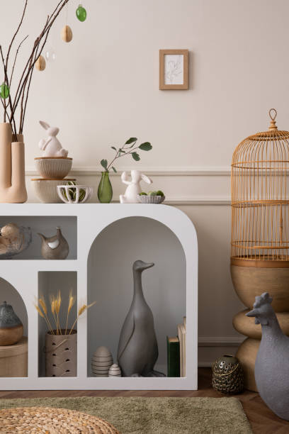 istock Creative composition of easter living room interior with mock up poster frame, white sideboard, colorful eggs, easter bunny sculpture, gray goose, hen and personal accessories. Home decor. Template. 1468218980