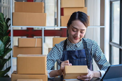 An Asian businesswoman enjoys his online SME business selling products, profiting from opening an online store, and taking orders for customer parcels inside the office. Concept SME Business.