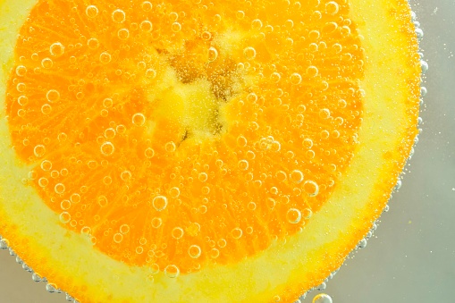 Close-up of an orange slice in liquid with bubbles. Slice of orange fruit in water. Close-up of fresh orange slice covered by bubbles.