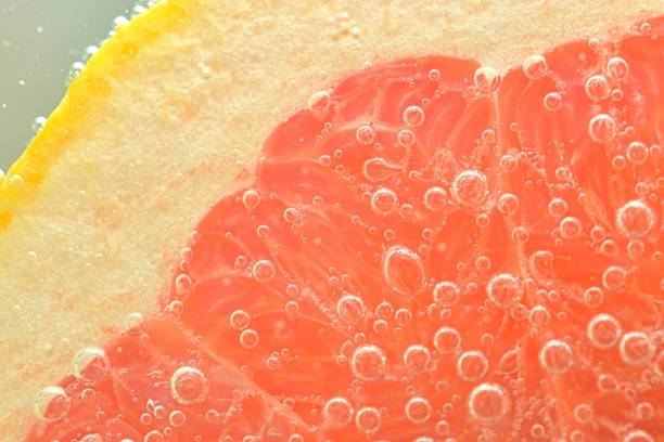 Close-up of fresh grapefruit slice on white background. Slice of red grapefruit in sparkling water on white background, close-up. Horizontal image stock photo