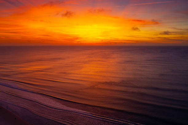 Daytona Beach sunrise seascape with glowing orange and red sun rays over the curving white waves at seashore in Florida, tranquil zen-like scenery, dramatic cloudscape of Atlantic Ocean during golden hour stock photo