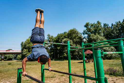 Handsome young mixed race man doing shoulder press exercises on the gym bars outdoors.