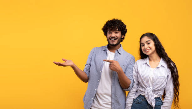 istock Cheerful indian couple pointing at open palm, man demonstrating invisible object, showing copy space, panorama 1468231236