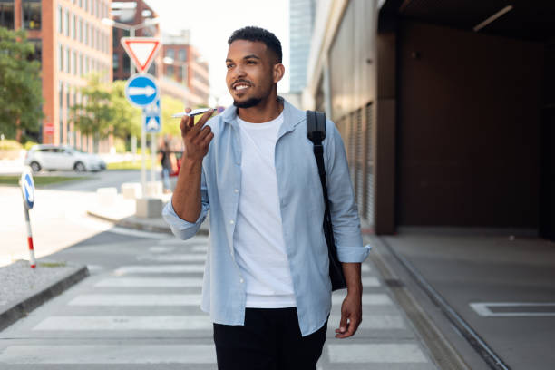 istock Handsome african american guy recording audio message on mobile phone, having conversation while walking in the city 1468231284