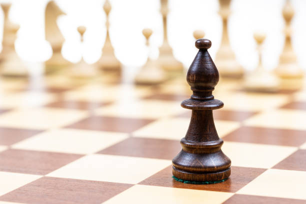 black bishop against white chess pieces on board stock photo