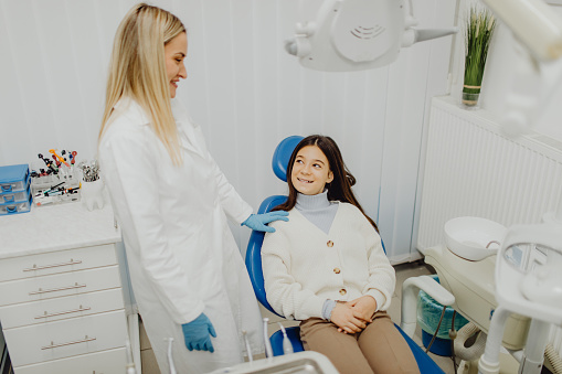 A young teenage girl sitting in the dental chair while her dentist is talking to her.