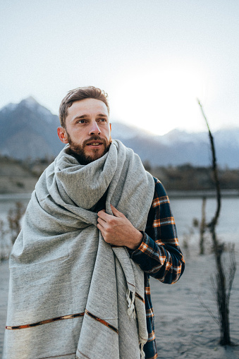 The portrait of a beautiful Caucasian male traveler wearing a traditional Pashtun shawl in the background of the scenic mountains at the sunset in Skardu, Pakistan