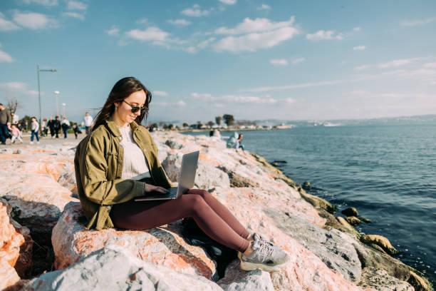 istock Business woman working on a laptop while sitting on a rock on the beach 1468237706