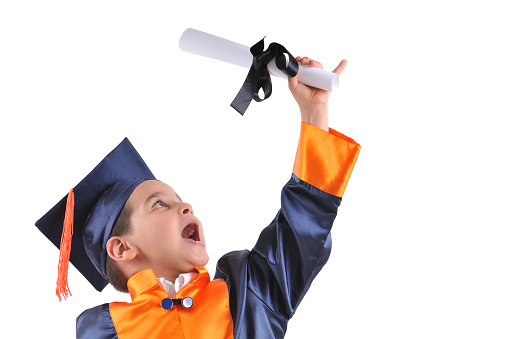 Cute boy in graduation uniform proudly holding his diploma up