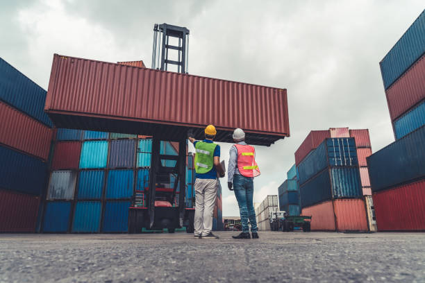 istock Industrial worker works with co-worker at overseas shipping container yard . Logistics supply chain management and international goods export concept . 1468240227