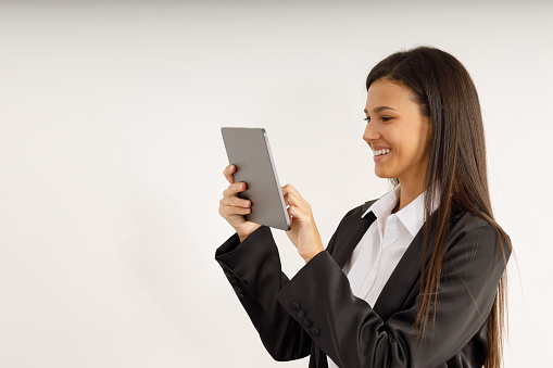 Portrait of successful business woman with tablet in her hands, dressed in white shirt and black jacket on isolated white background. Studio shot of attractive brunette girl