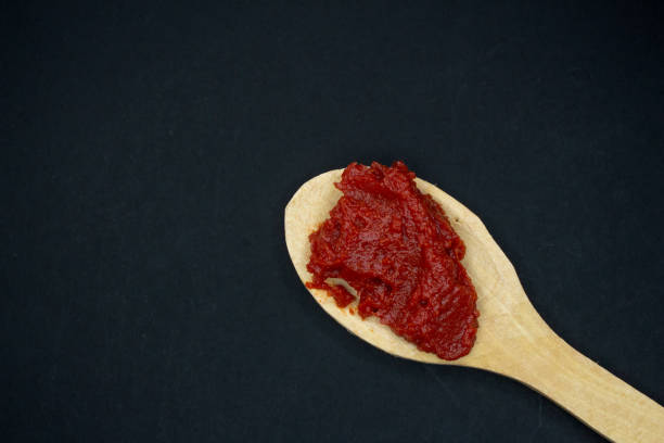 Wooden spoon with tomato paste on a black background. Top view, copy space.