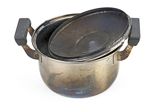 A stainless steel pot with burnt marks lid from being left on the stove on white background. Black burns on stainless steel pots occur when they are left on the stove for too long.
