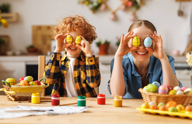 istock Happy mother and little son sitting at table in kitchen and covering eyes with Easter eggs 1468242580