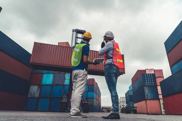 istock Industrial worker works with co-worker at overseas shipping container yard . Logistics supply chain management and international goods export concept . 1468243613