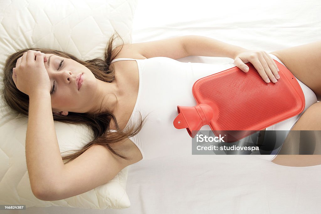 Woman with hot water bottle on stomach Young woman lying on bed with hot water bottle on her stomach Hot Water Bottle Stock Photo