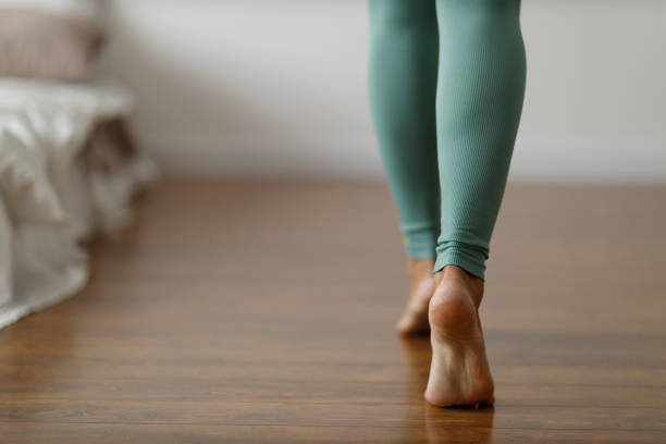 Young woman in sports leggings walks barefoot on the warm floor in the bedroom. Close-up of cropped image of barefoot girl. Underfloor heating system wood panels stock photo
