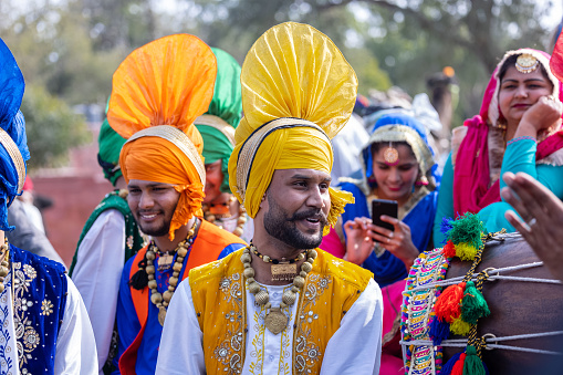 Bikaner, Rajasthan, India - January 2023: Punjabi Bhangra, Portrait of young sikh male in traditional punjabi colorful dress and turban performing bhangra dance with smile in camel festival with selective focus.